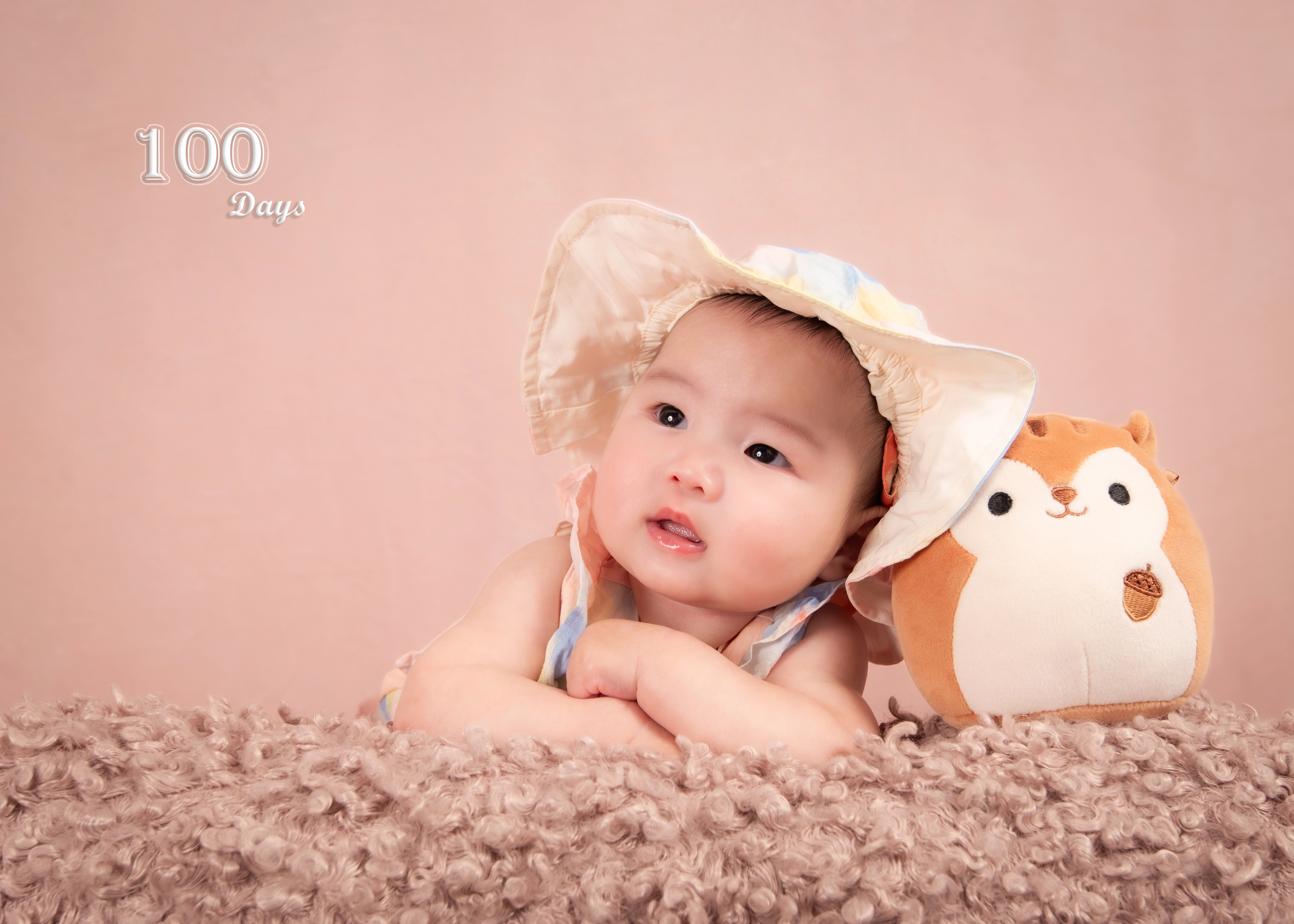 100-day milestone baby in sunhat leaning on soft fur with chipmunk plush — peach backdrop — Edmonton baby photography
